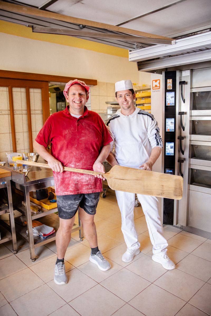 Zwei Bäcker mit Brotschieber vor den Backöfen der Backstube