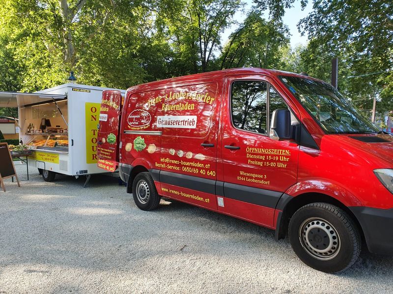 Roter Lieferwagen mit Verkaufsanhänger unter Bäumen